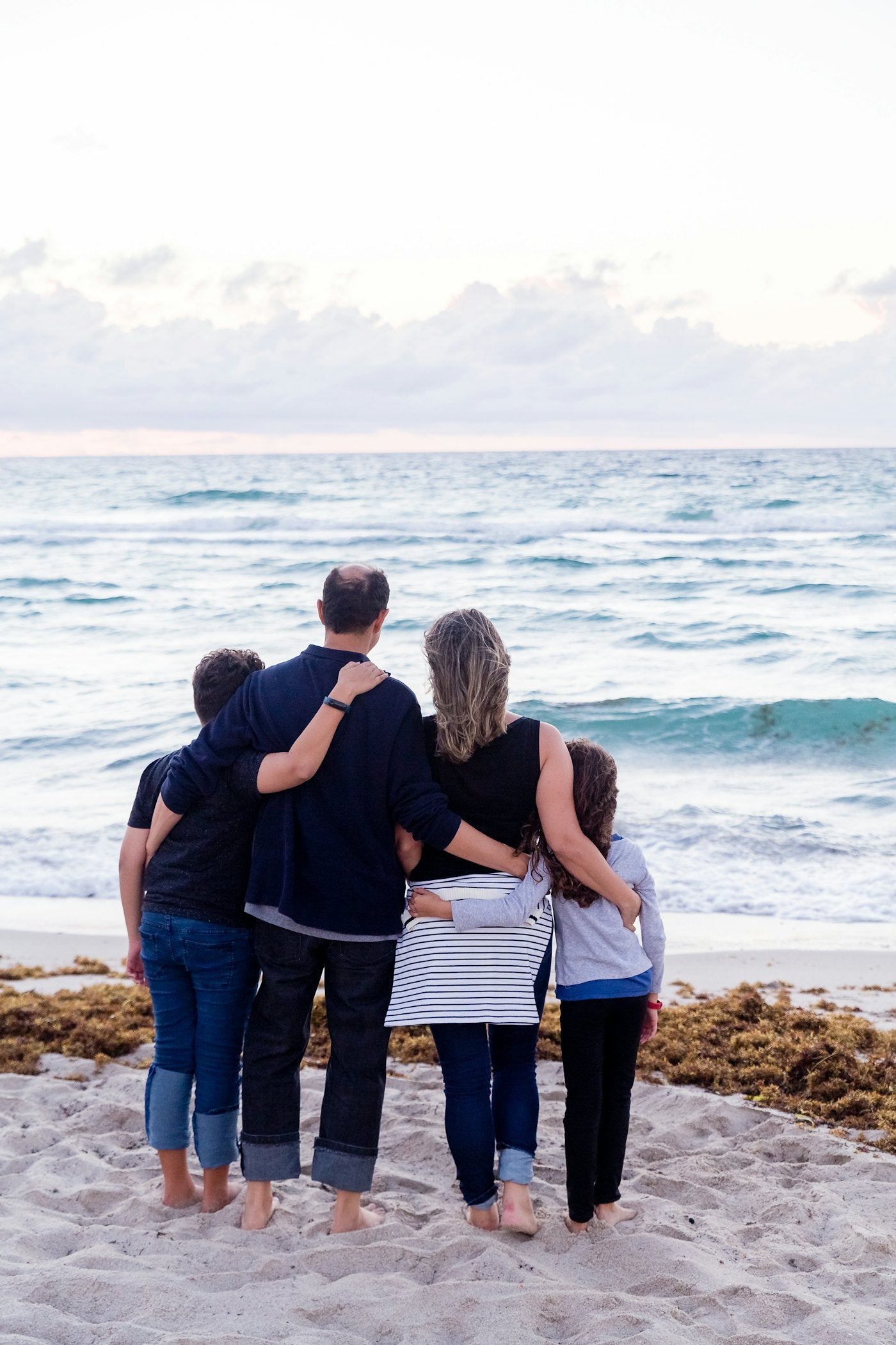 A family of four with arms around each other on the beach